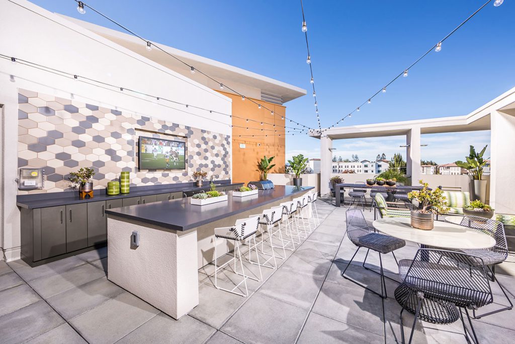 Sunnyvale, CA Apartments - Community Sky Deck with TV, Long Bar, Tables, Seating, and Aesthetic Lighting.